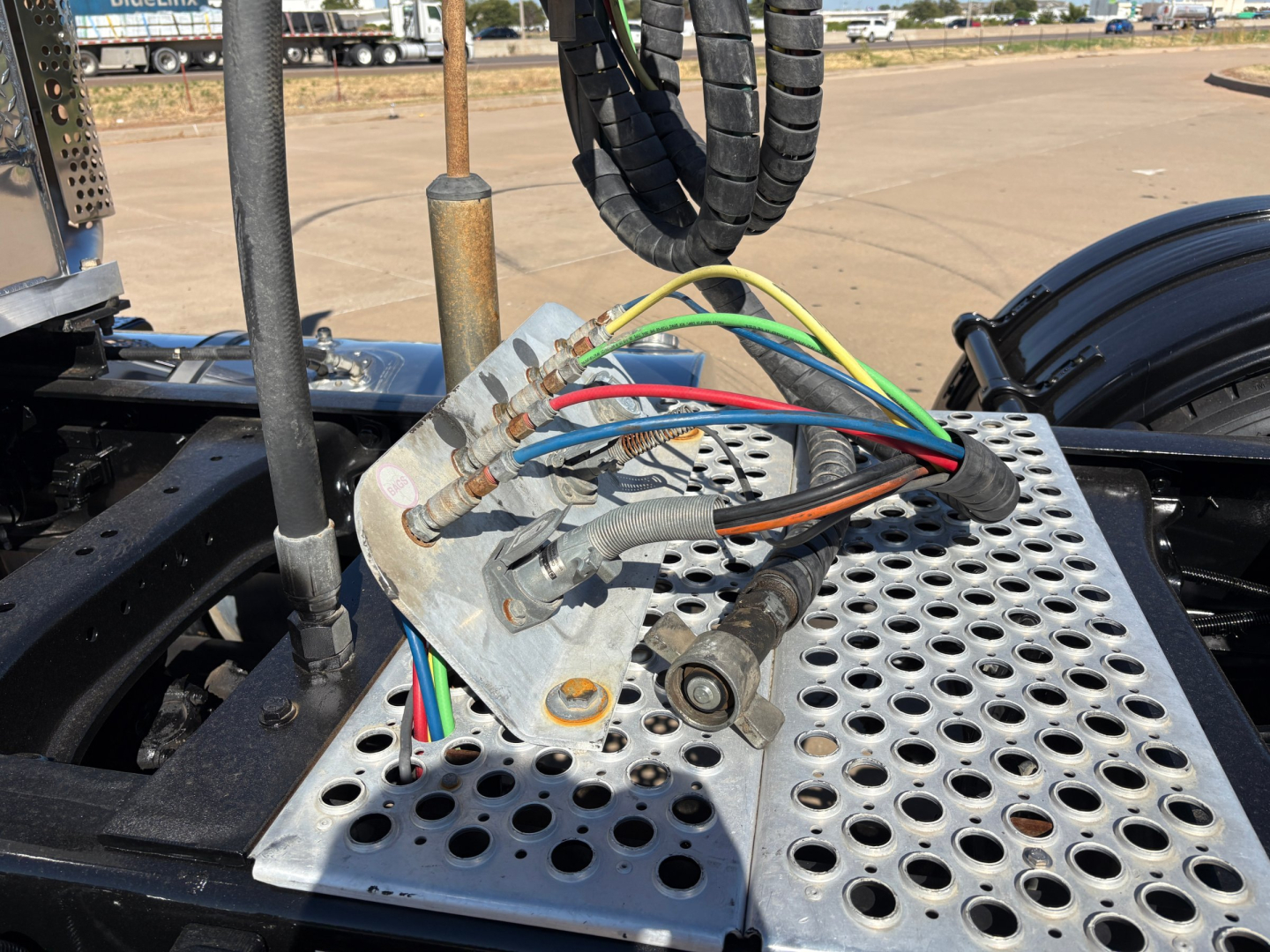 Kenworth T880 chassis area with a perforated metal step and a terminal block with multicolored wires connected to metal lugs.