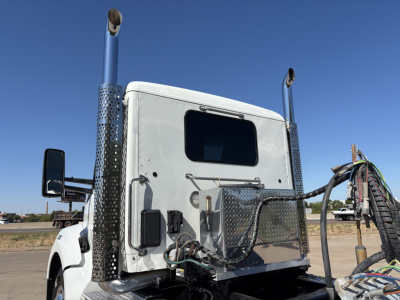 Kenworth T880 conventional daycab truck rear/view showing tall exhaust stacks with perforated heat shields and chain-link guards, side mirror, and wiring harness in view.