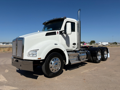 Kenworth T880 conventional daycab tractor in white with chrome exhaust stack and dual rear axles, side view showing cab mirrors and front grille.