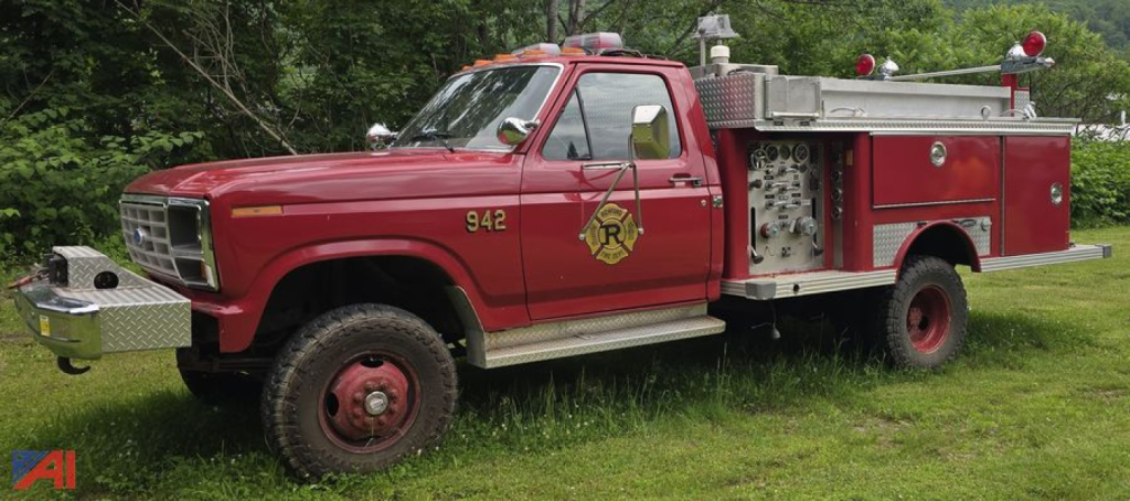 Ford F-350 brush fire truck in-service showing emergency lights, 942 on front fender, side compartment with pumps, red with gold badge.