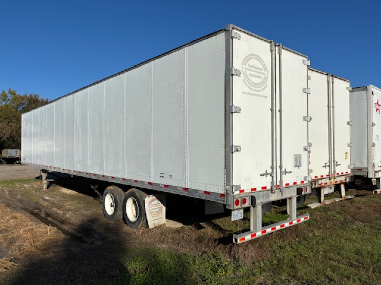 Trailer side and rear showing long rectangular cargo trailer with tandem axles and double doors.