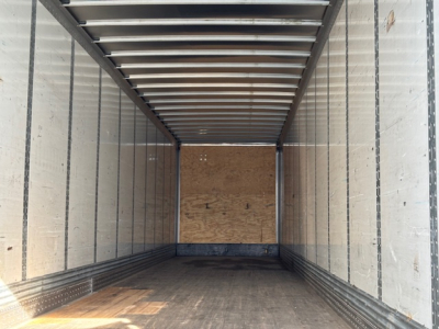 Trailer interior showing metal walls and wooden floor, empty cargo space with side rails and roof supports.