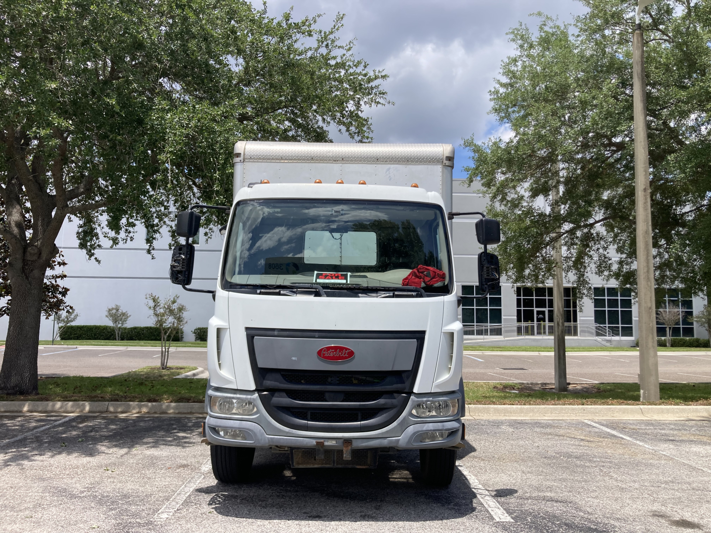 Peterbilt 220 cabover truck head-on view with silver grille and white cab, in a parking lot.