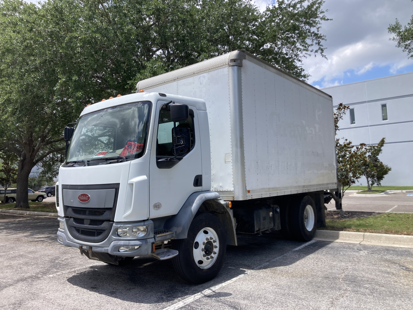 Peterbilt 220 cabover truck with box body in a parking lot, front-left view showing cab and cargo area.
