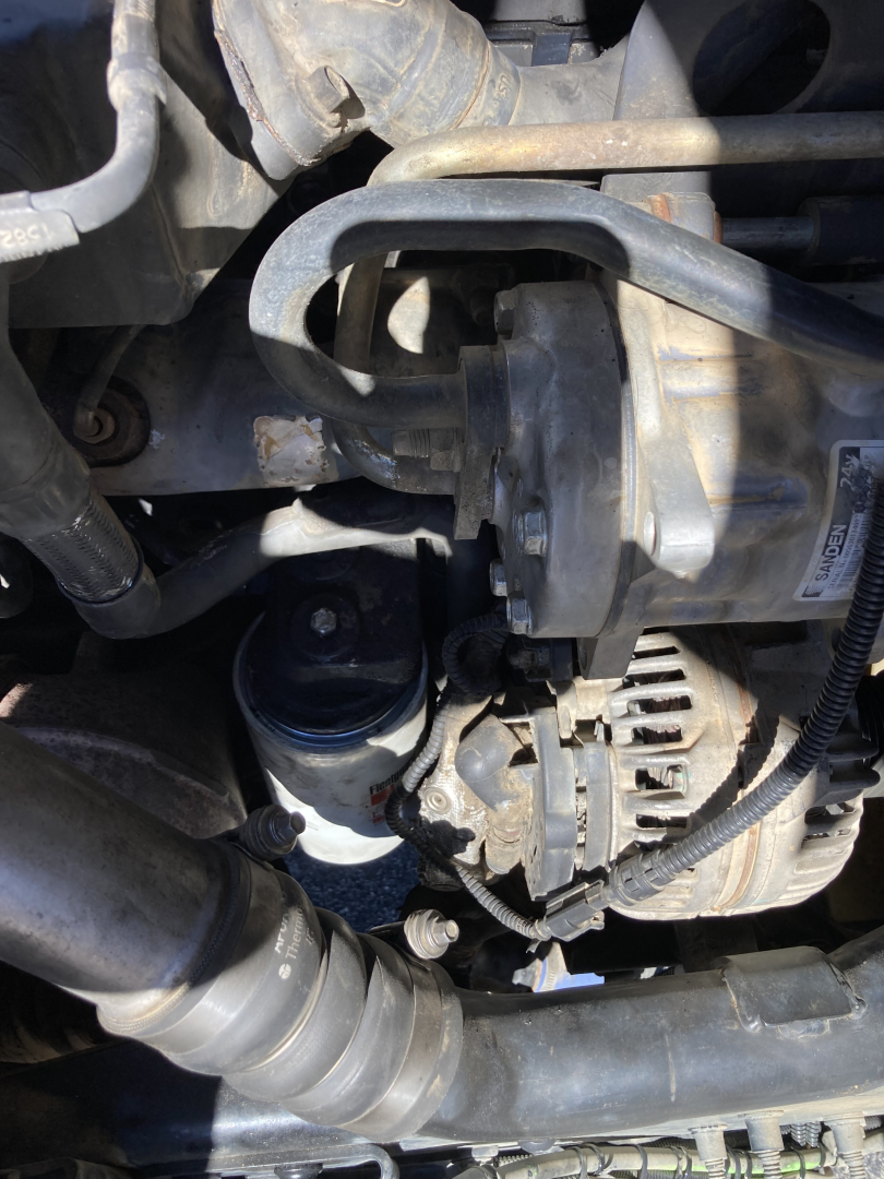 Peterbilt 220 engine bay showing alternator, hoses, and reservoir; visible components include an electrical connector and various engine tubing.