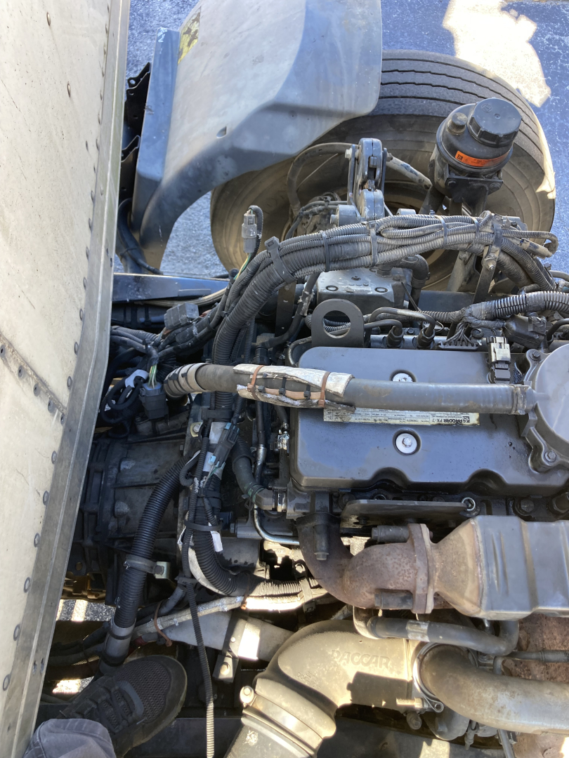 Peterbilt 220 cabover engine bay/view showing diesel engine components, hoses, wiring harness, and coolant reservoir.
