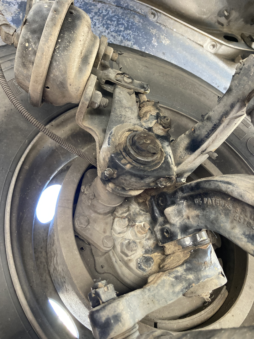 Front axle and steering components of a 2017 Peterbilt 220 cabover showing wheel hub, suspension linkage, and brake rotor with dirt and grime.