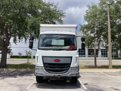 Peterbilt 220 cabover truck head-on view with silver grille and white cab, in a parking lot.