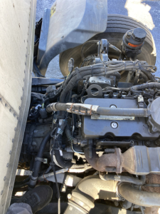 Peterbilt 220 cabover engine bay/view showing diesel engine components, hoses, wiring harness, and coolant reservoir.