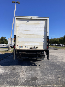 Rear view of a white Peterbilt 220 box truck with a large cargo door, bumper, and license plate area; no visible branding legible.