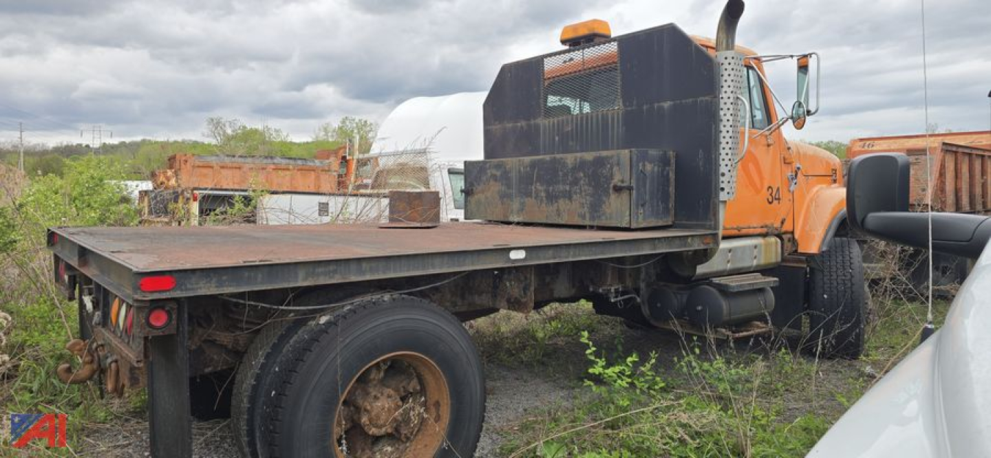 Flatbed dump truck showing rear cab and flatbed platform with dual rear wheels and exposed frame.