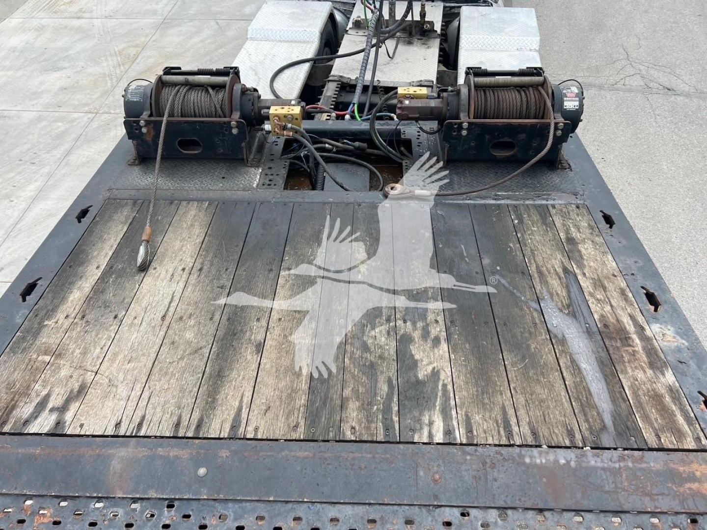 Truck trailer hitch area with wooden deck and two winches, cables, and pulleys; top view of deck revealing weathered wood and mechanical winches.