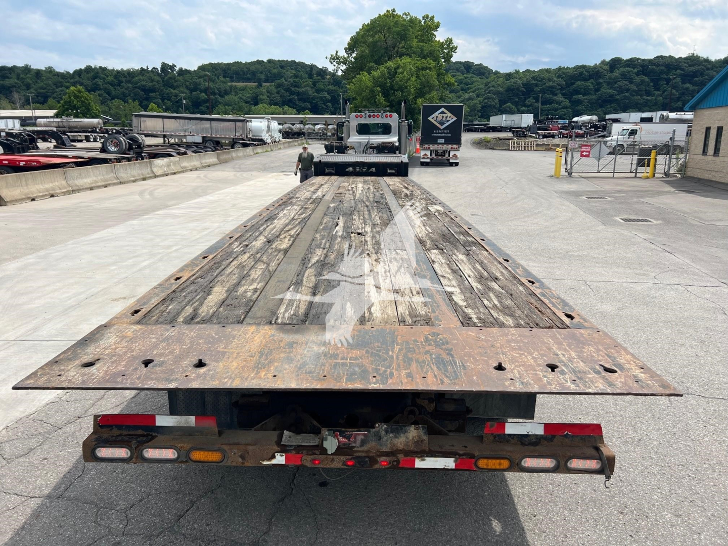 Flatbed trailer with long wooden deck and metal ramp sections; visible wear and rust on the end gates; Landoll 455A-53 model trailer in a yard.