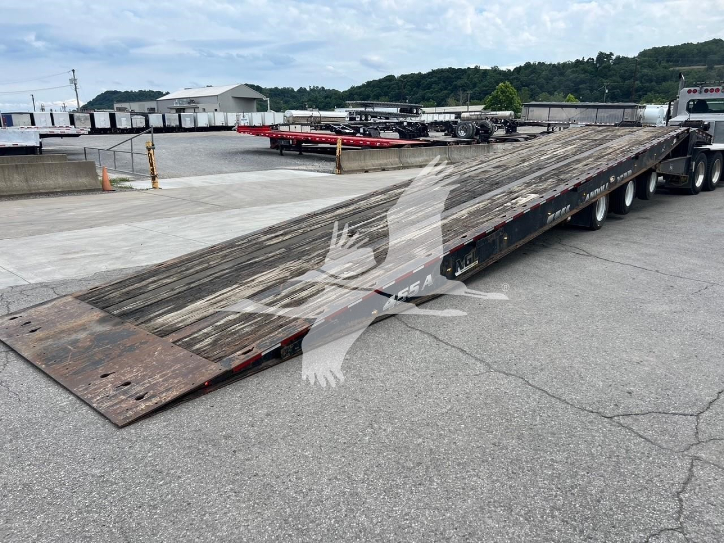 Long flatbed trailer from a Landoll 455A-53 with weathered wooden deck and multiple axles, in a parking lot.