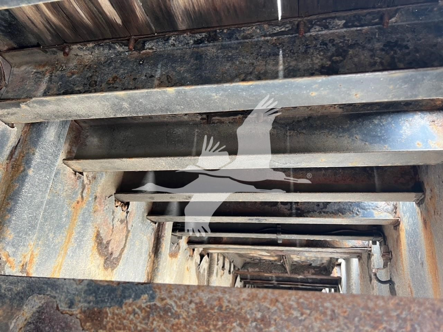 Traveling axle trailer interior with stacked metal beams and rusted supports; view down a rectangular, perforated frame showing structural members.