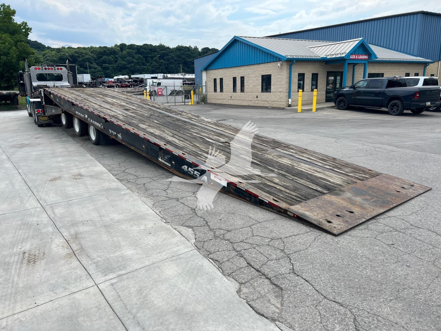 Landoll 455A-53 lowboy trailer in serviceable condition with long ramp sections extended, parked in lot near blue-roofed building.
