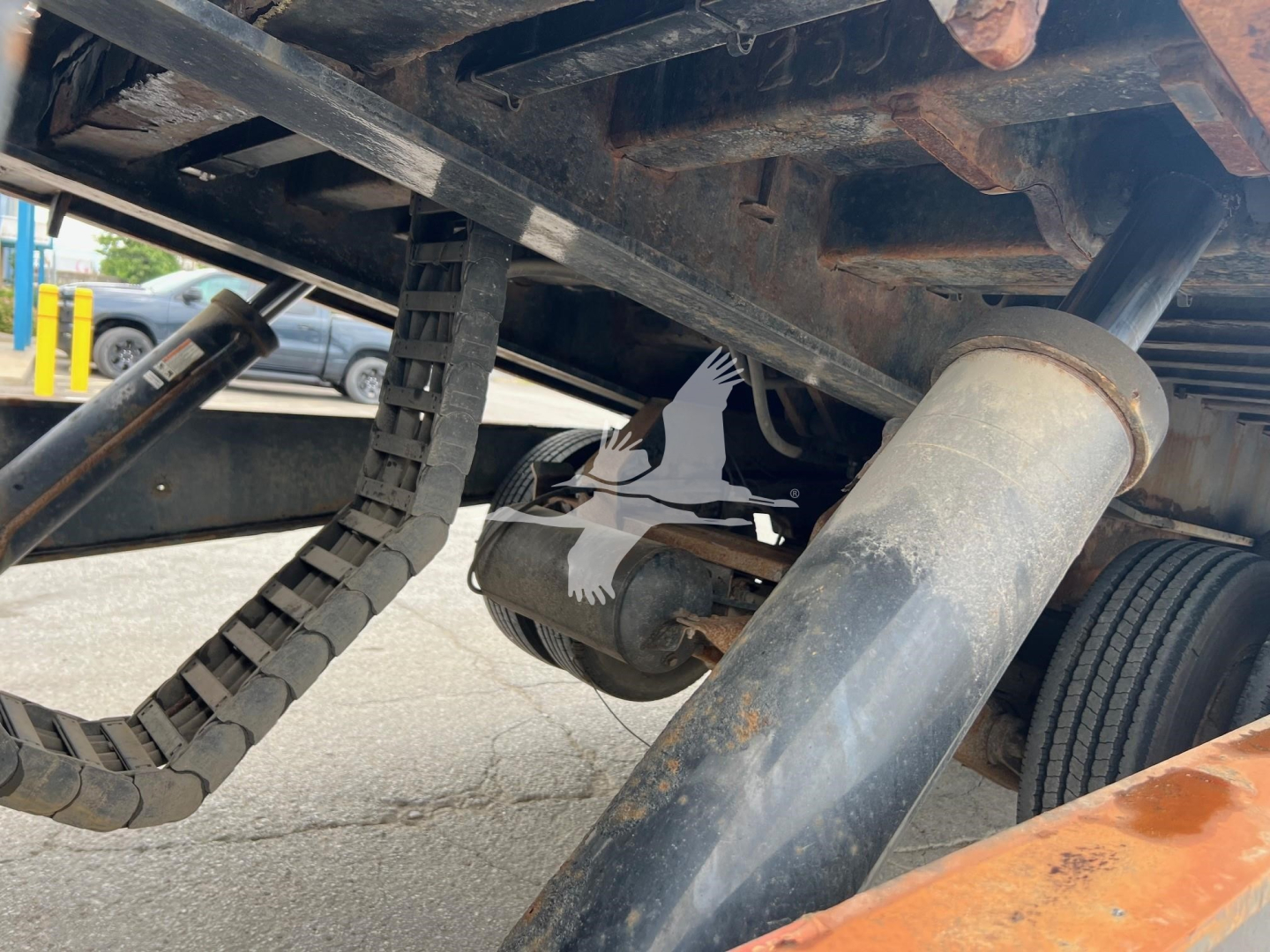 Landoll trailer undercarriage showing hydraulic cylinder and wiring harness near wheel assembly, with chain and structural members visible.