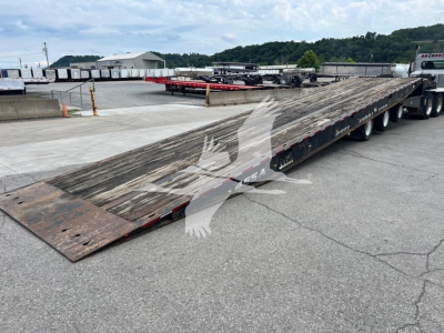 Long flatbed trailer from a Landoll 455A-53 with weathered wooden deck and multiple axles, in a parking lot.
