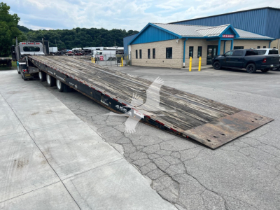 Landoll 455A-53 lowboy trailer in serviceable condition with long ramp sections extended, parked in lot near blue-roofed building.