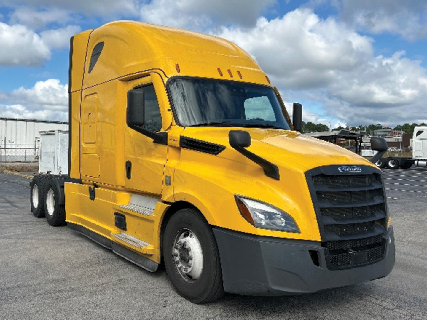 Truck cab in bright yellow with black grille and large mirrors, Freightliner Cascadia style sleeper tractor, front-left view.
