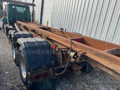 Mack RD688S roll-off truck chassis showing orange flatbed with multiple axles and tires.