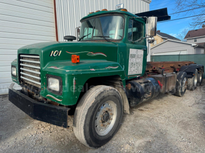 Mack RD688S roll-off truck showing green cab with number 101 and white decals, single front axle, dual rear axles, mounted on a gravel lot.