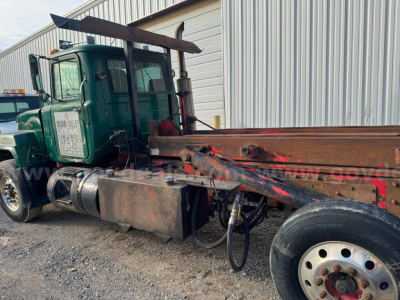 Truck chassis with green Mack RD688S cab and roll-off body showing exposed hydraulic lines and frame components.