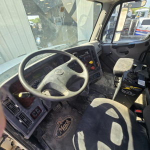 Interior of a Freightliner truck cab showing steering wheel, dashboard, and gear shifter; dirty floor mat with logo; driver and passenger seats; visible controls and panels.