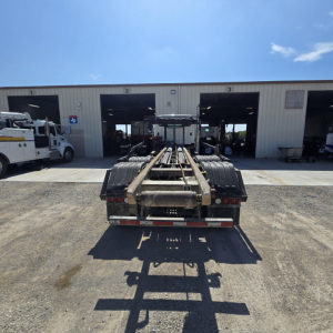 Rear view of a Freightliner roll-off truck chassis in a service yard showing connection frame and rear lights.