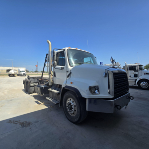 Truck cab and chassis of a Freightliner 114SD roll-off truck, side view, white exterior, front grille, and exhaust stack visible.