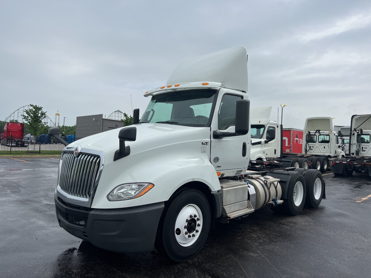 Truck showing International LT cab and front grille with dual rear axles, white exterior and tall sleeper, fuel tanks along side, tires, and side mirrors.