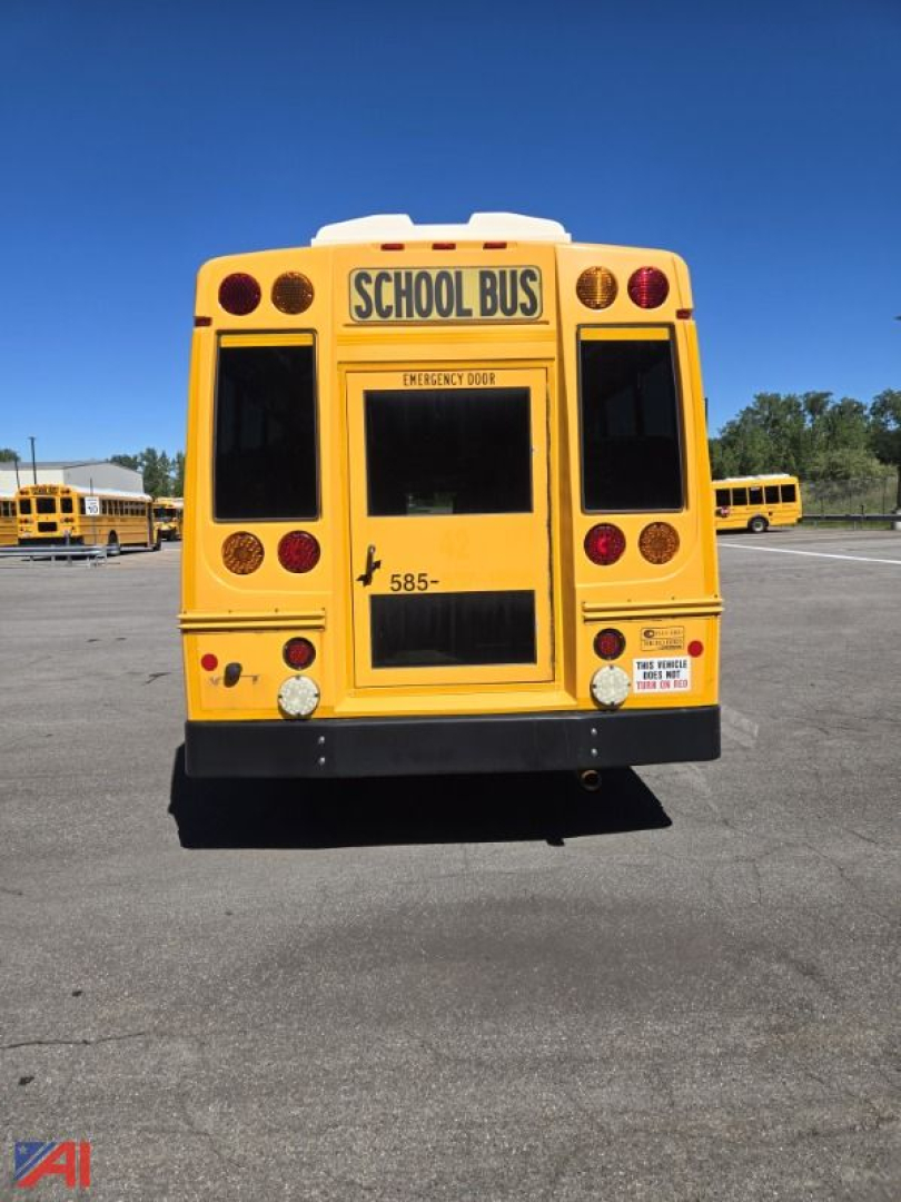 Rear view of a yellow school bus with 'SCHOOL BUS' sign above the rear window, emergency exit sign, and various circular red reflectors and lights.
