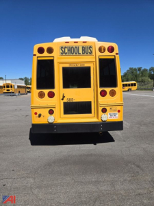 Rear view of a yellow school bus with 'SCHOOL BUS' sign above the rear window, emergency exit sign, and various circular red reflectors and lights.