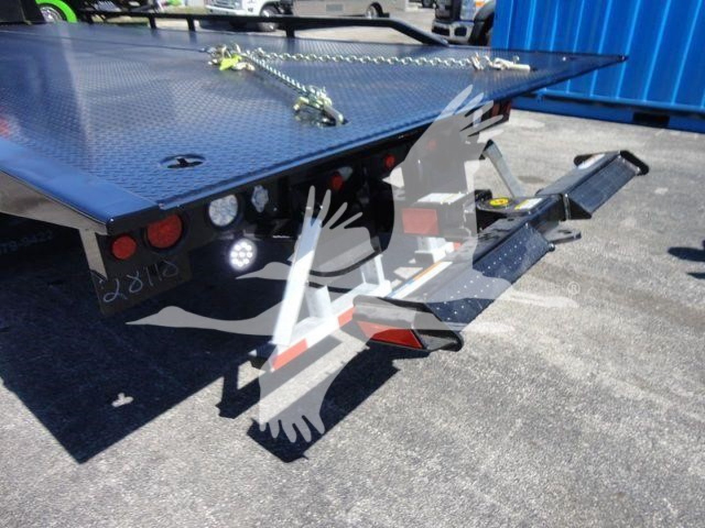 Truck flatbed with a ramp and hydraulic lines, showing rear of a 2024 Ram 5500 SLT in a dealership lot.