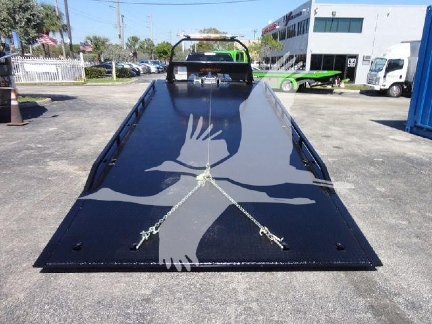 Ram 5500 rollback flatbed showing glossy black surface and safety chains, front cab visible in distance.