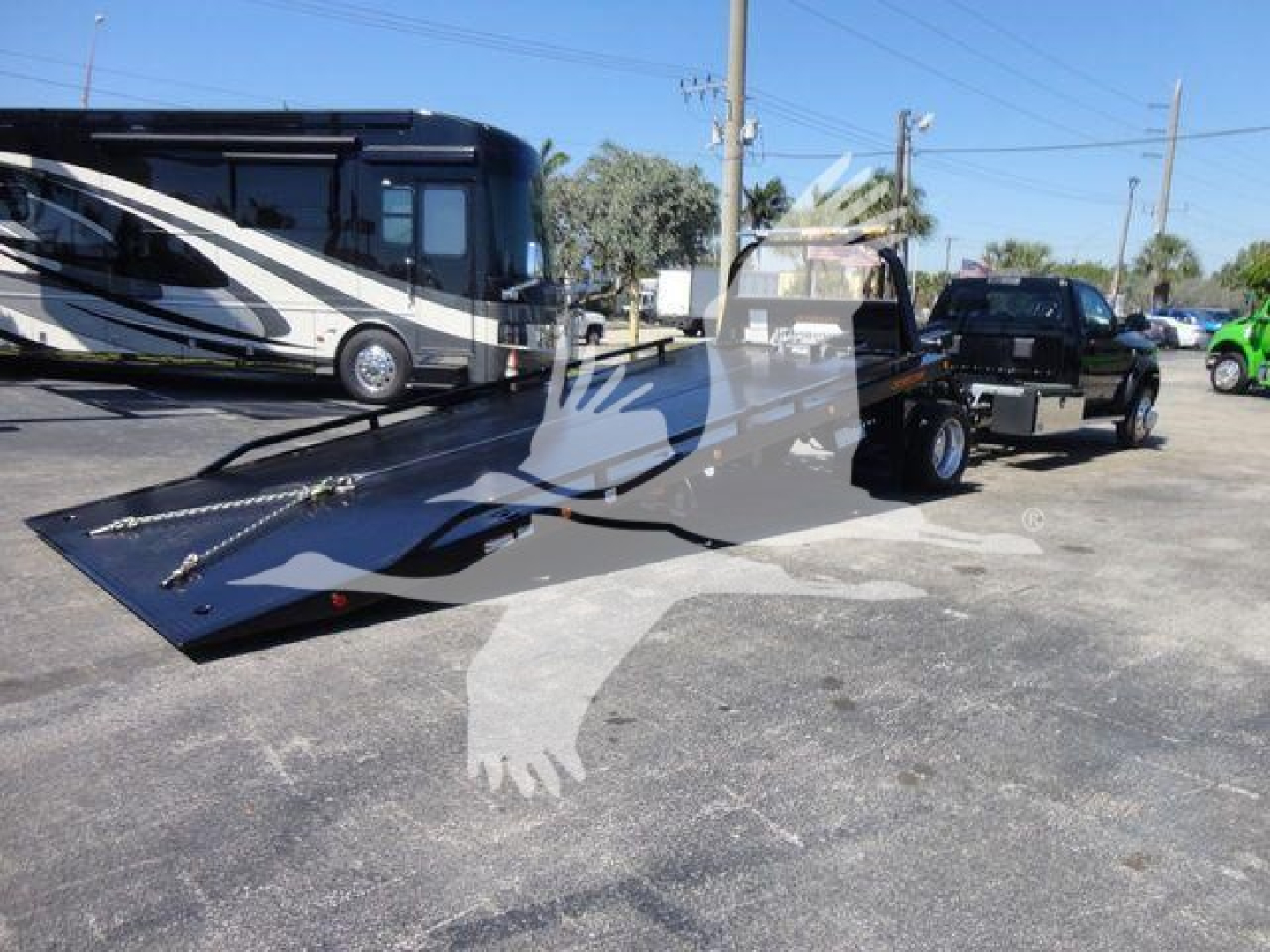 Ram 5500 rollback tow truck in a parking lot with a long black flat-bed and a tow hitch, stock number J24797, new condition.