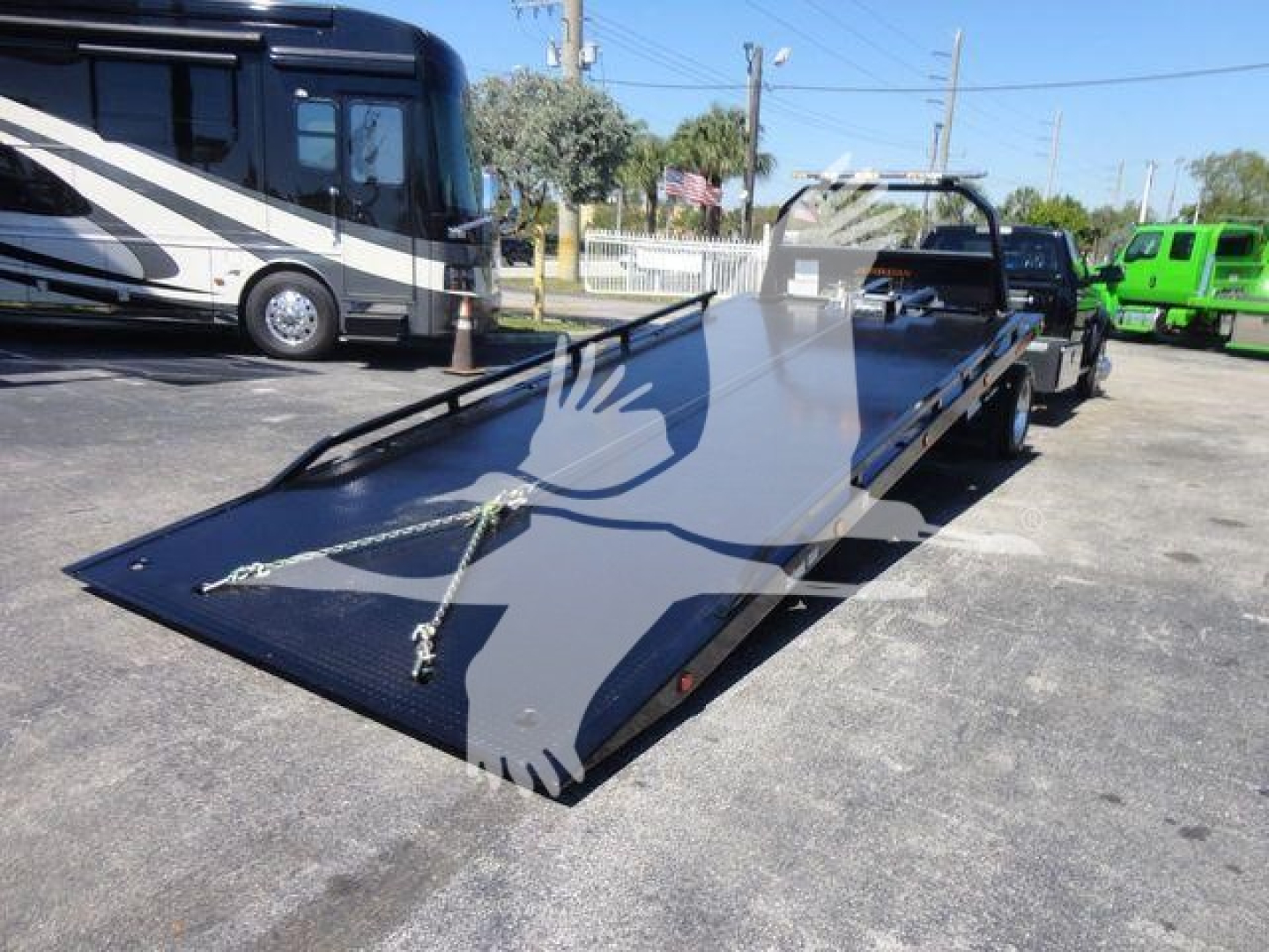 Ram 5500 rollback flatbed tow truck in new condition with long flatbed and wheel chocks, side rails, and mirrored footage in the lot.