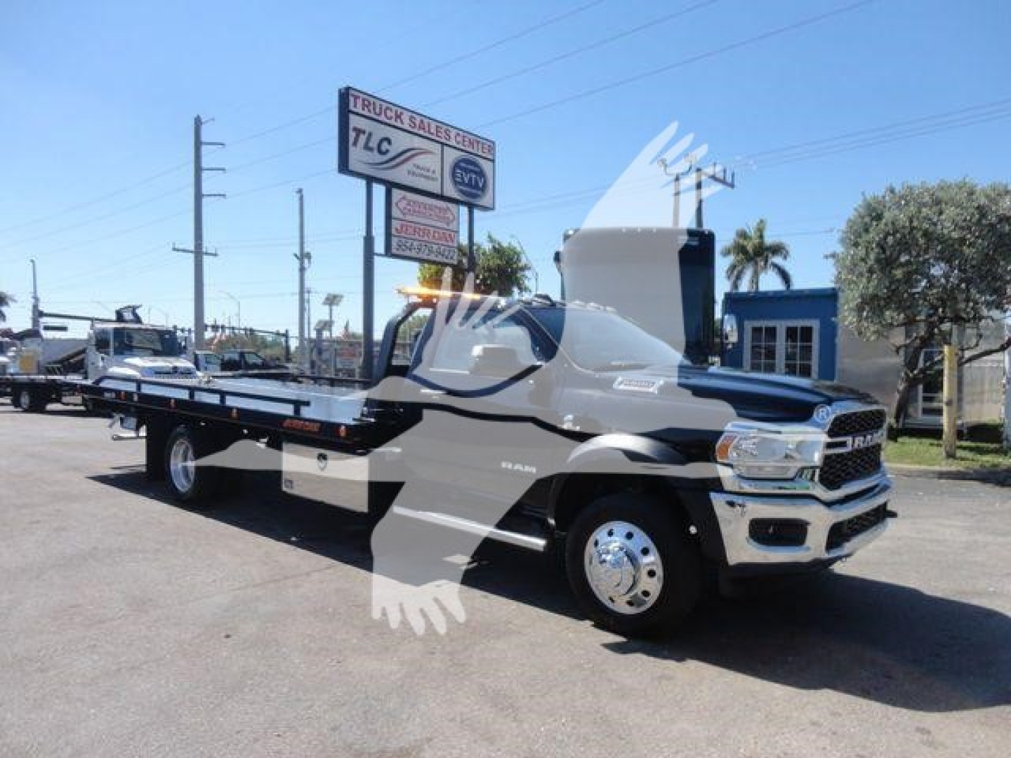 Ram 5500 rollback truck in a dealership lot with a white cab and flatbed, front grille and wheel visible, signage in background.