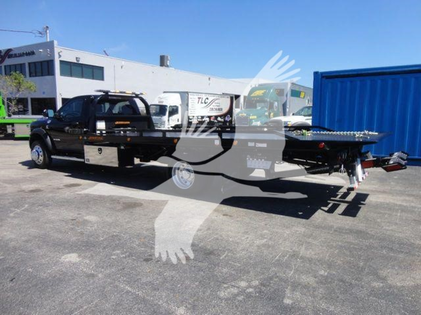 Tractor-style pickup truck with a flatbed and rollback trailer attached, black color, showing two-tone diamond plate toolboxes on the side, in a dealership lot.