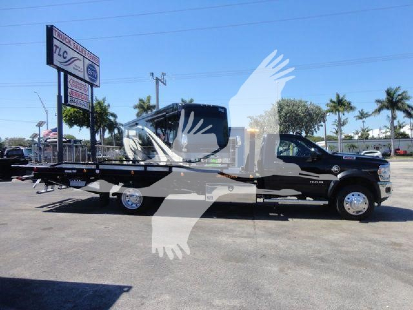 Ram 5500 SLT tow truck with rollback bed in a dealership lot, side view, black cab and flatbed, palm trees in background.