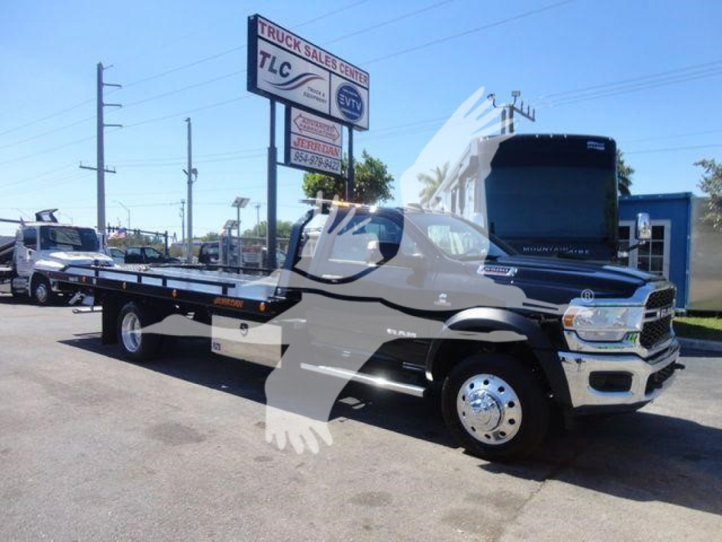 Ram 5500 rollback tow truck shown in profile with open flatbed and raised hood, dealership lot in background.