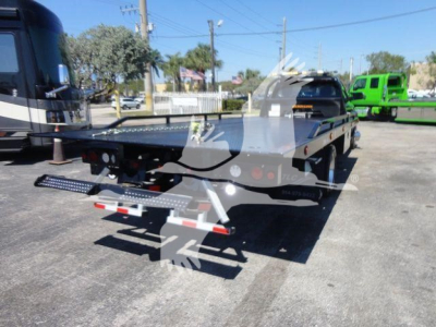 Ram 5500 rollback flatbed tow truck with dual rear ramps viewed from rear-left side showing metal flatbed and fold-out ramps.