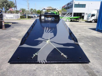 Ram 5500 rollback flatbed showing glossy black surface and safety chains, front cab visible in distance.
