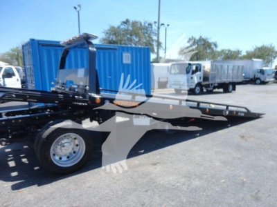 Ram 5500 rollback tow truck flatbed chassis visible with blue container and other trucks in background.