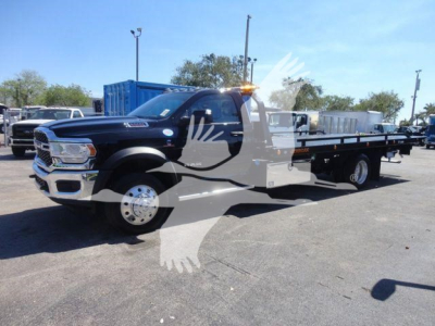 Ram 5500 rollback truck showing black cab and long flatbed with warning beacon, side mirrors, and dual rear wheels.