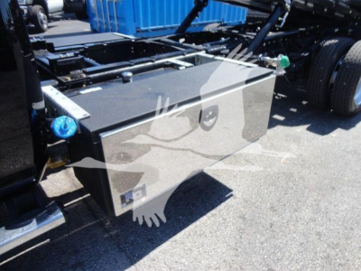 Truck chassis with a large underframe toolbox or storage box mounted, showing a black metal rectangular box attached to the side of the frame near the cab. There are hoses and components nearby.