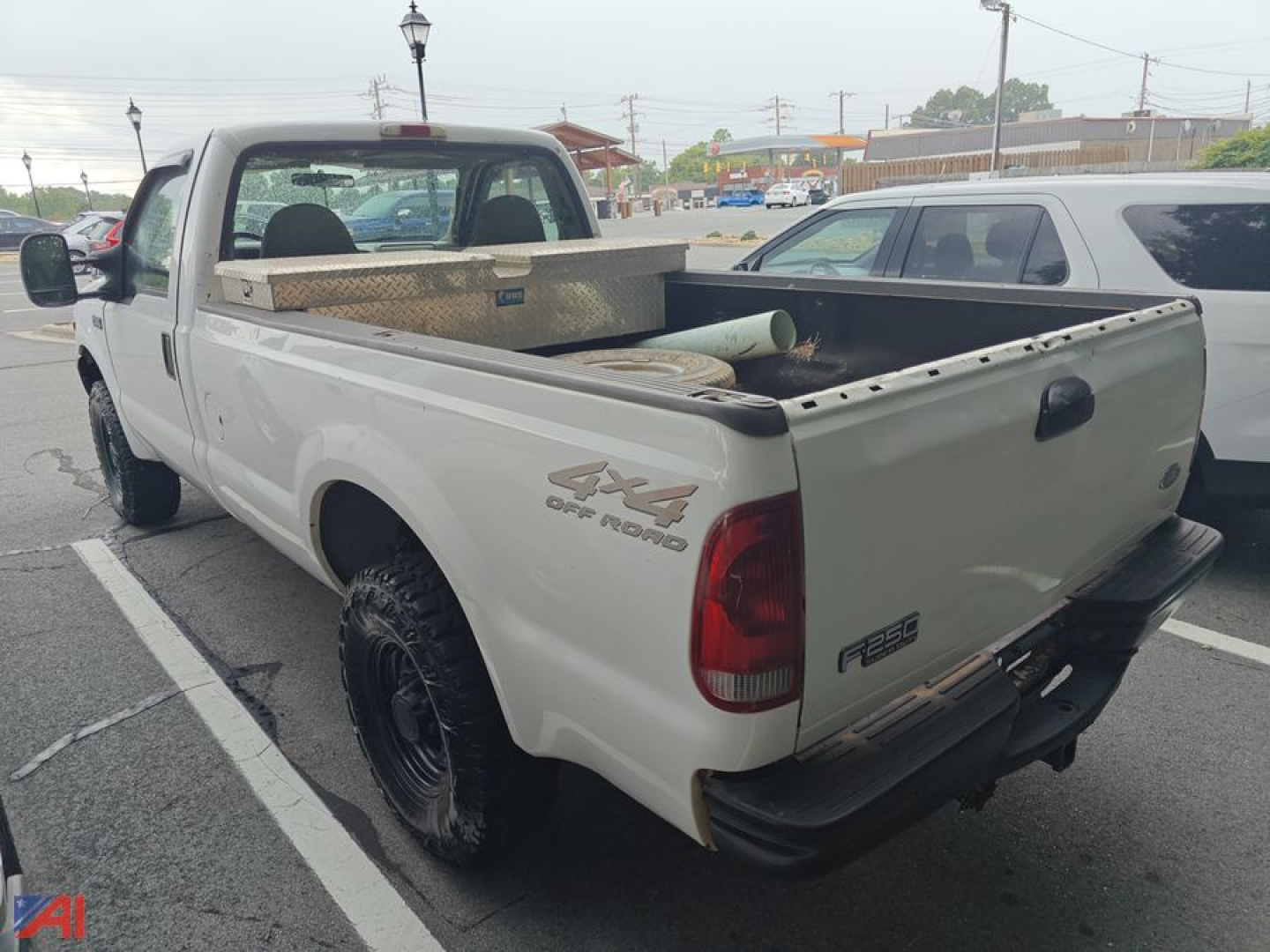 Ford F-250 pickup truck 4x4 with open bed seen from rear-left side; white exterior, toolbox in bed, aftermarket dual rear wheels, visible tailgate and badge.