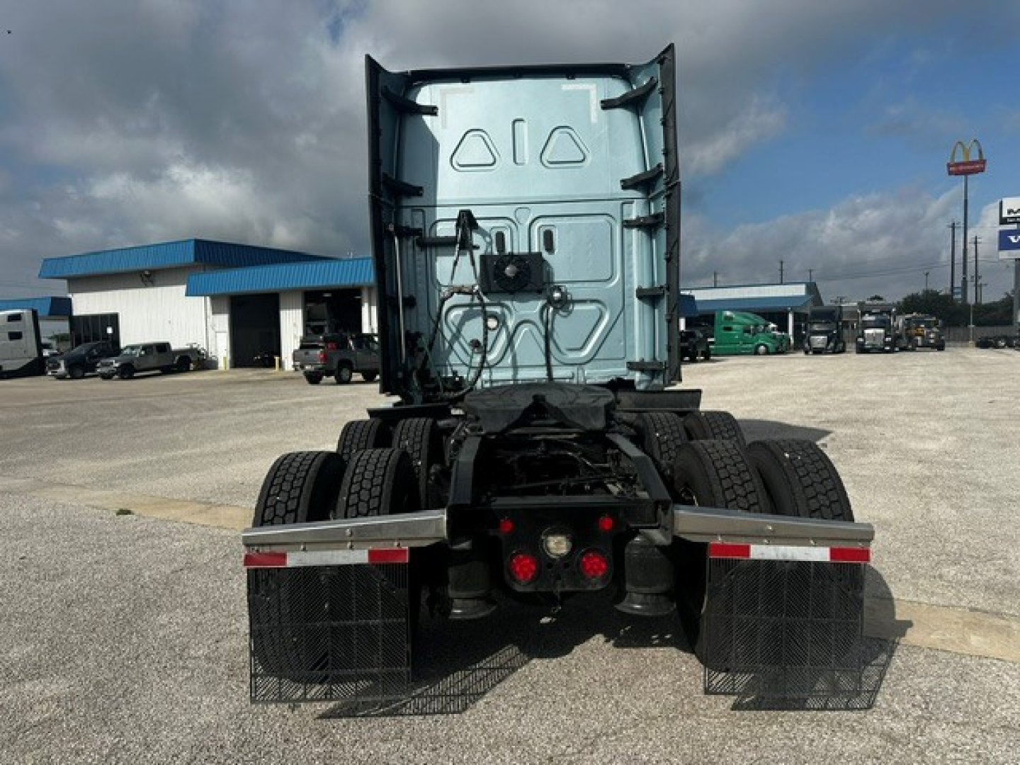 Semi truck rear view showing fifth wheel and dual rear axles with mud flaps and taillights.