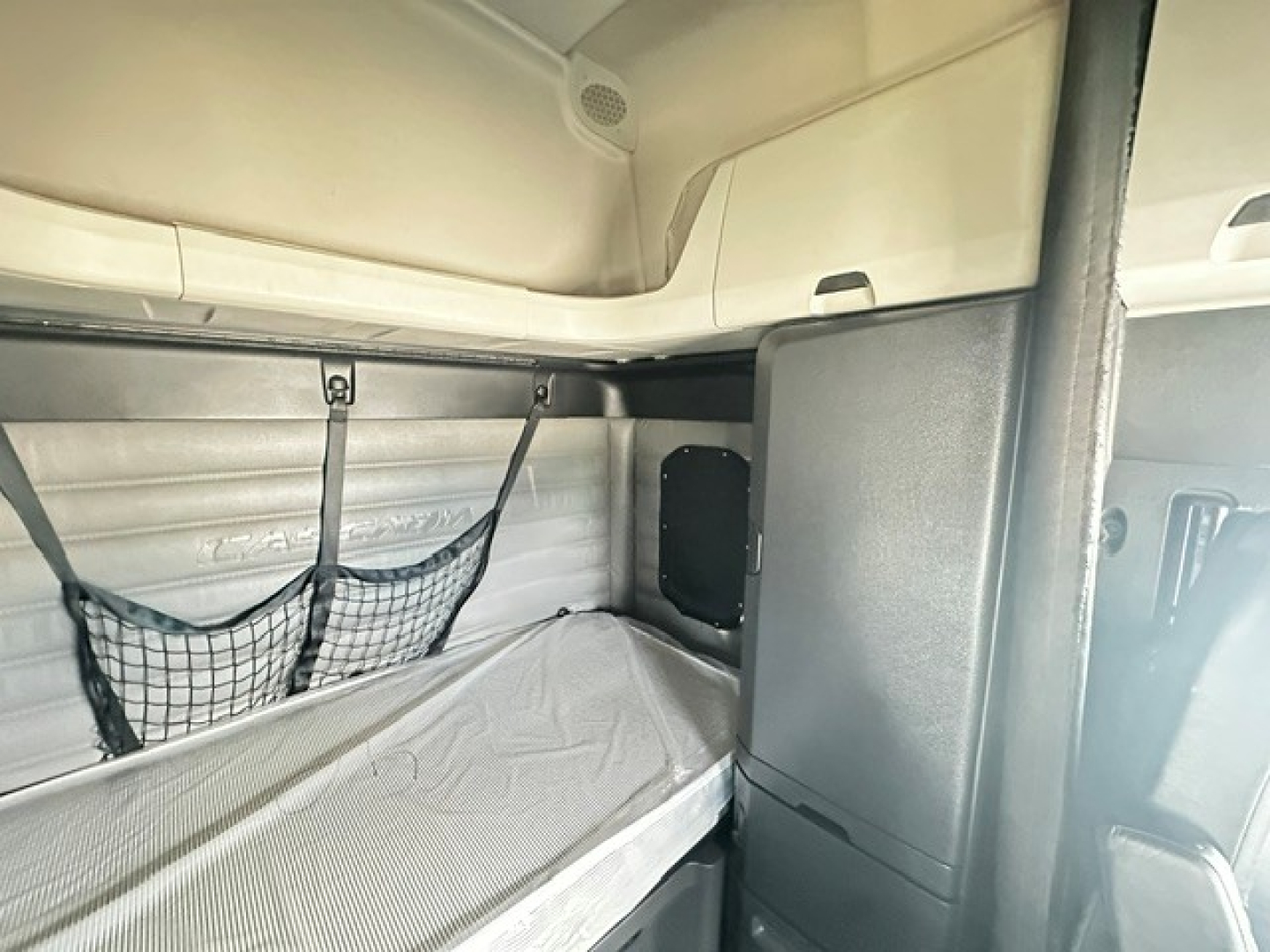 Cab interior of a Freightliner Cascadia 126 sleeper showing bunk bed with net storage and storage cabinet.