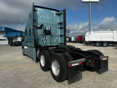 Truck rear view showing cab and dual rear axles, blue Freightliner Cascadia 126 tractor, fifth wheel area, mud flaps, and luggage compartments.